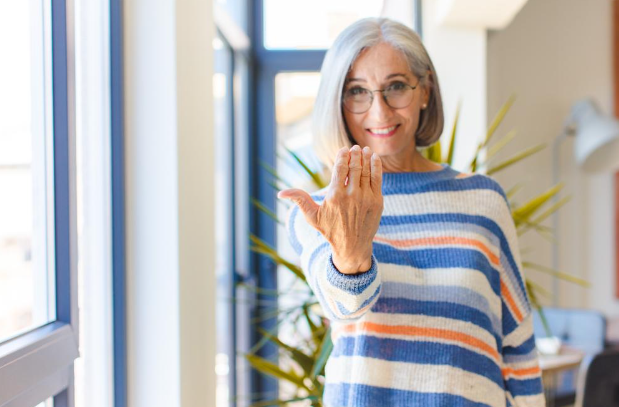 An older woman with a smile on her face. Her hand is extended out motioning for you to come closer.